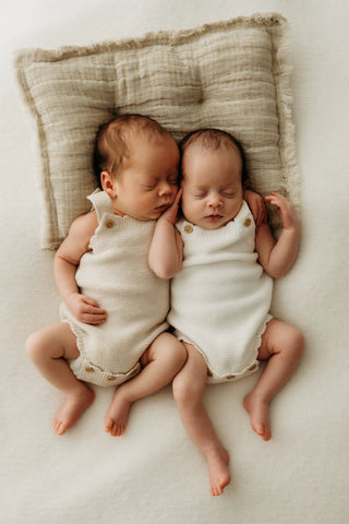 Sleeping baby twins lying on a cushion wearing neutral knitted rompers