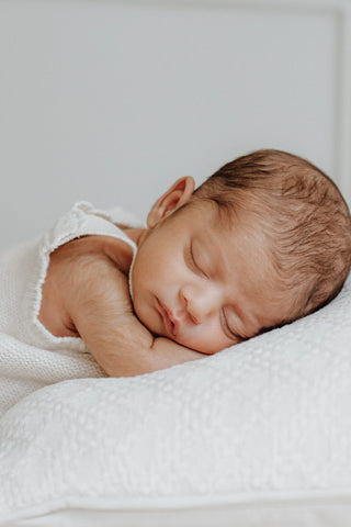 Sleeping baby lying on a cushion wearing a white knitted romper