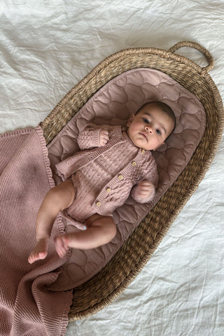 Baby in moses basket wearing knitted pink outfit with pink basket liner and pink blanket